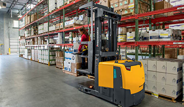 Worker strapped to Jungheinrich high-level order picker carrying a box